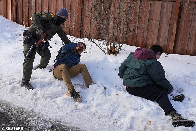 A federal agent retains protesters trying to block vehicles in the streets of Minneapolis