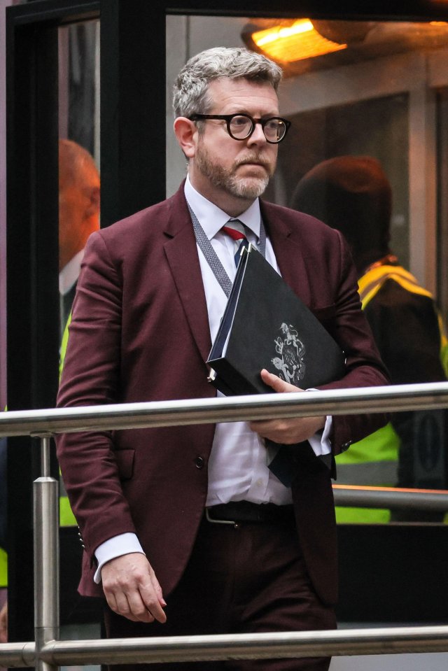 Matthew Doyle, Starmer government Director of Communications, wearing a maroon suit and glasses, holds a black binder.