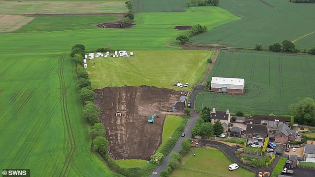 An excavator can be seen tearing up the grass, with caravans already parked on the far end of the plot