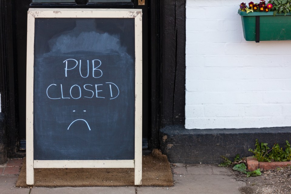 Chalkboard sign on a pub door reads "PUB CLOSED" with a sad face drawn below, indicating closure due to the COVID-19 pandemic.