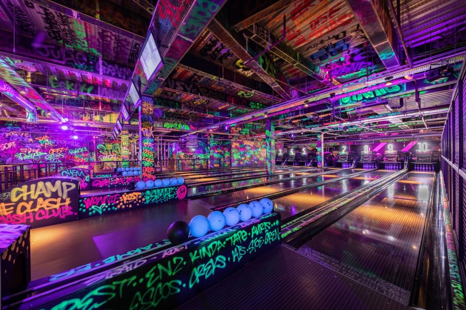 A neon-lit bowling alley with graffiti-covered walls and lanes.