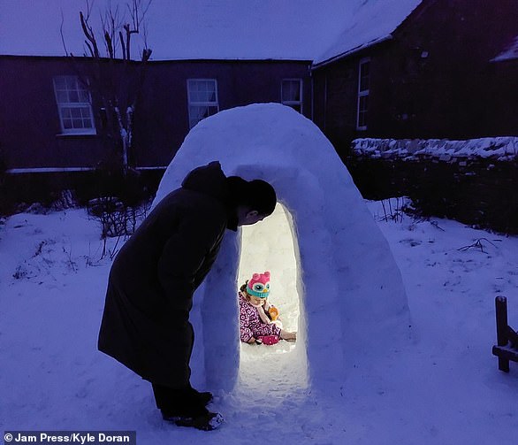 Kyle Doran looks at his daughter Norah inside the igloo he created in his garden