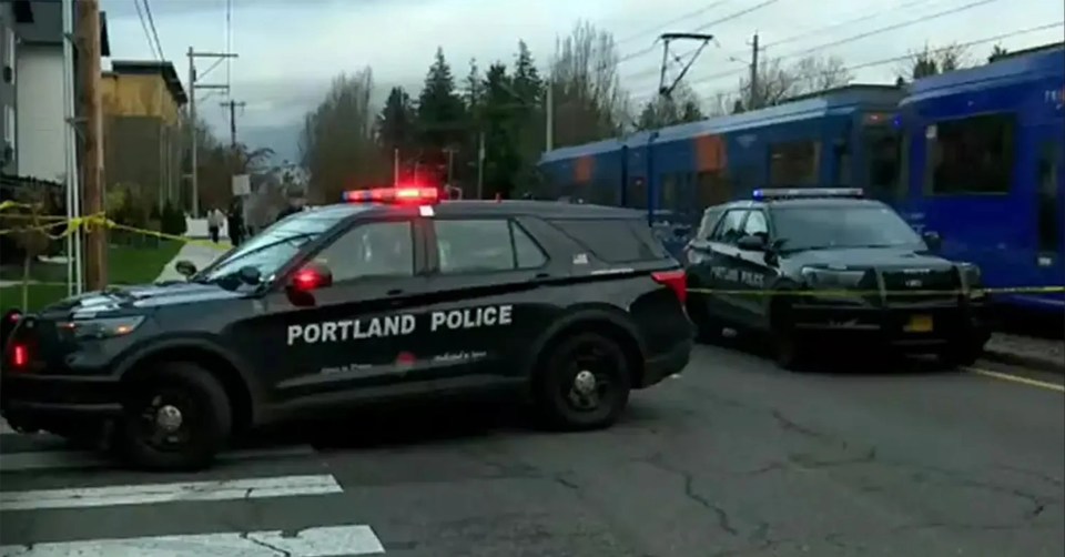 Two Portland Police cars with flashing lights on a street next to a blue train.