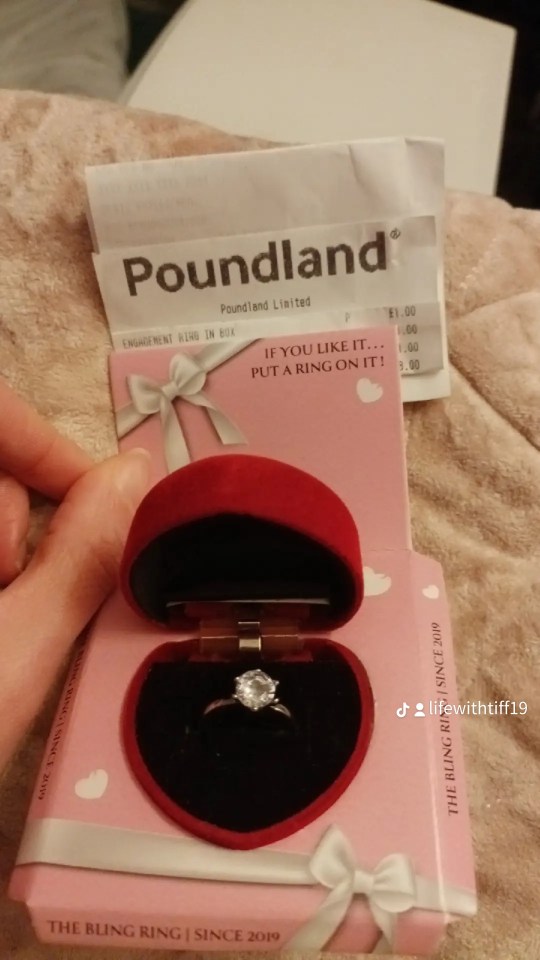A Poundland receipt for an "Engagement Ring in Box" costing £1.00 next to an open heart-shaped red ring box revealing a silver ring with a large clear gem.