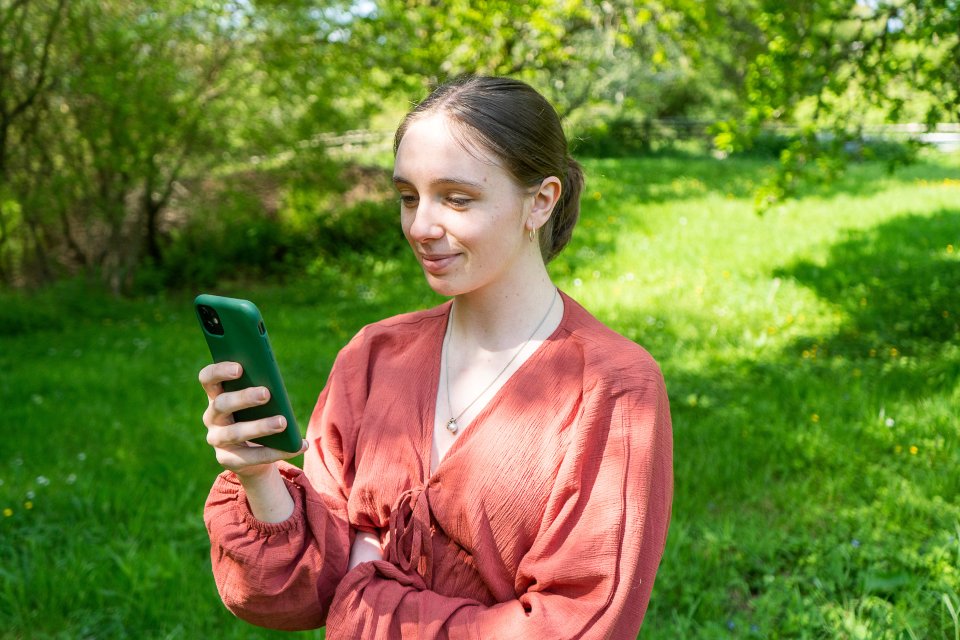 Woman in a coral shirt smiling while looking at a green-cased smartphone.