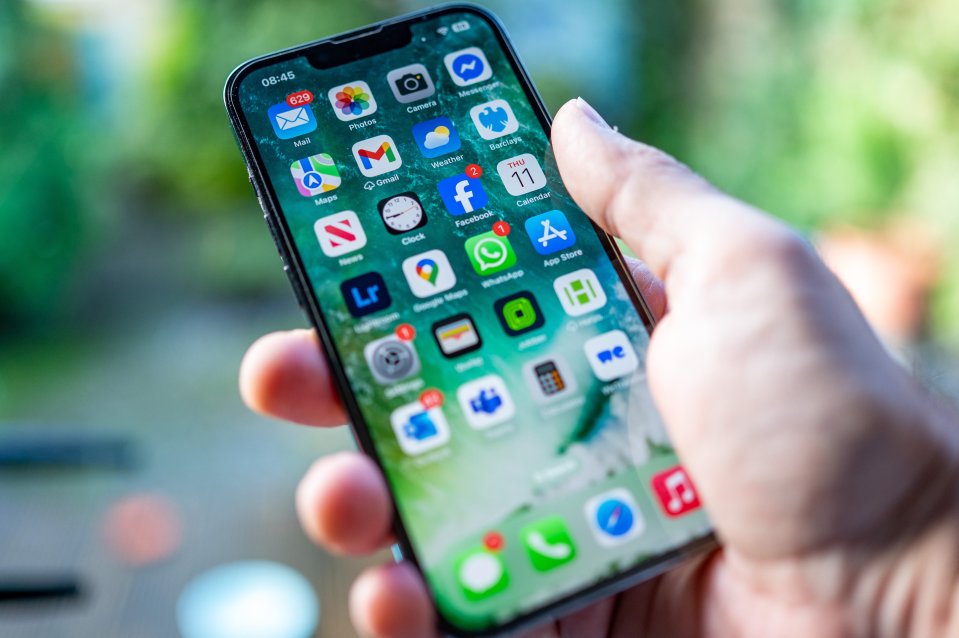 Hand holding an iPhone displaying various app icons and notifications, including 629 new emails and 2 Facebook notifications.