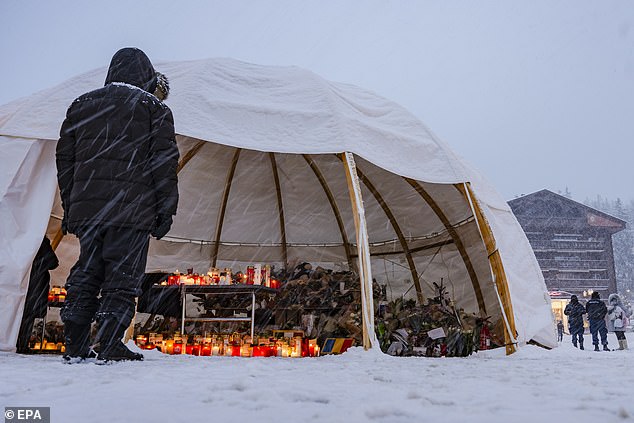 Mourners stand in front of a tent sheltering flowers and candles left in tribute to the victims following a bar fire in Crans-Montana, Switzerland, January 8, 2025
