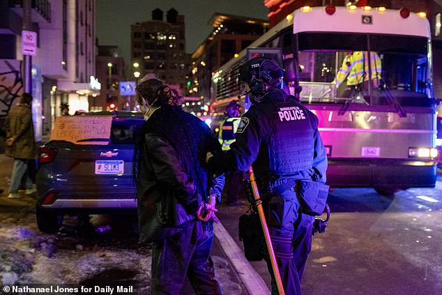One masked demonstrator is seen in handcuffs being escorted off the street