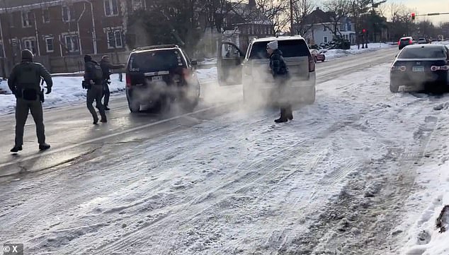 Ross (pictured to the left of the SUV) is seen holding his pistol up as the vehicle drives off