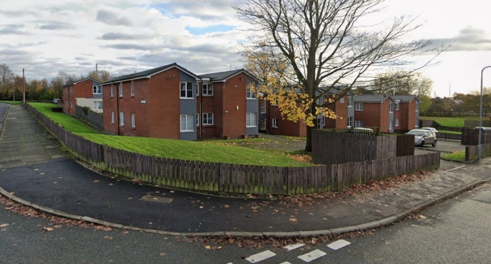 Gerards Court in St Helens, a residential area with red brick buildings, green lawns, and a wooden fence along the road.