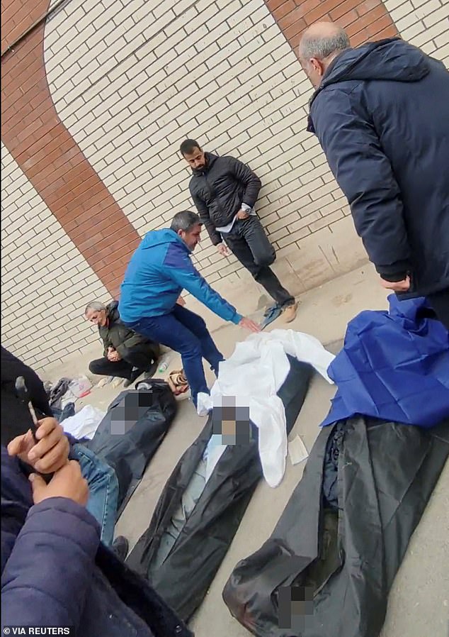 Mourners look shellshocked as they cover the faces of loved ones outside the medical centre