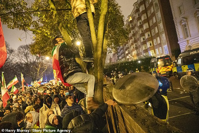 Police try to stop protesters climbing the outside wall toward the Iranian Embassy in London on January 11, 2026