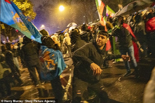 A protester throws an object toward the Iranian Embassy as they clash with police in London this evening as anti-government demonstrations intensified