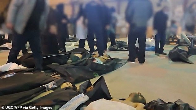 People are seen walking by bodies in body bags laid out in a large room, attempting to identify them
