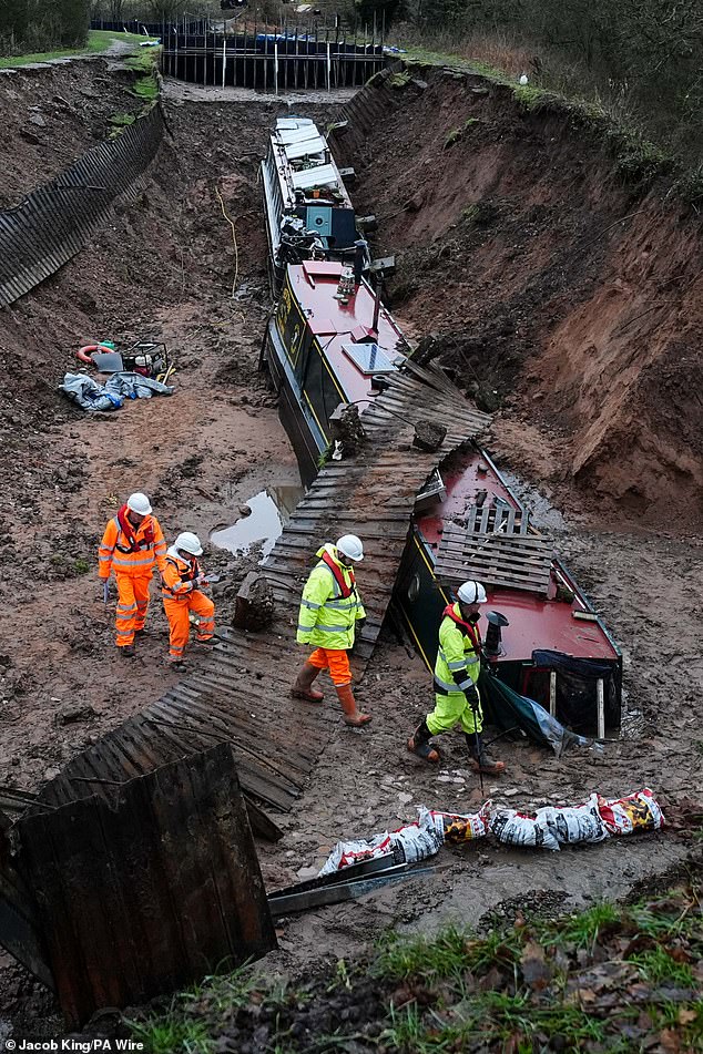 Waterways engineers inspect an area where two boats remain within a large 'sinkhole' which breached a canal in the Chemistry area of Whitchurch