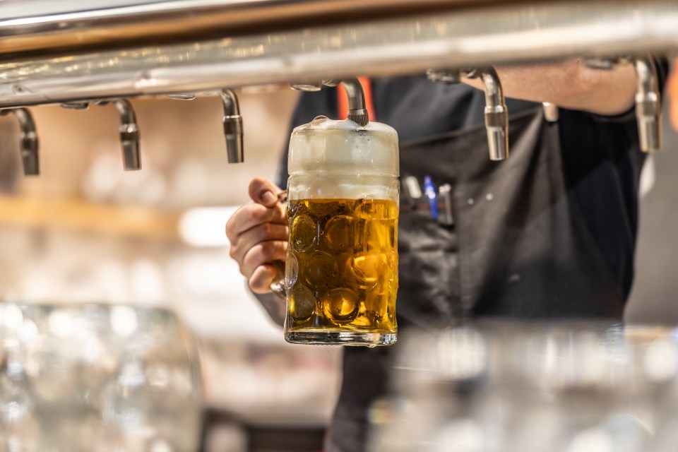 A close-up of the bartender's hand holding a pint glass at an angle as it is being filled with lager, captures the moment of a beer being poured into a pub.