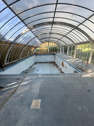 An eerily empty indoor swimming pool is littered with dirt and leaves at the property
