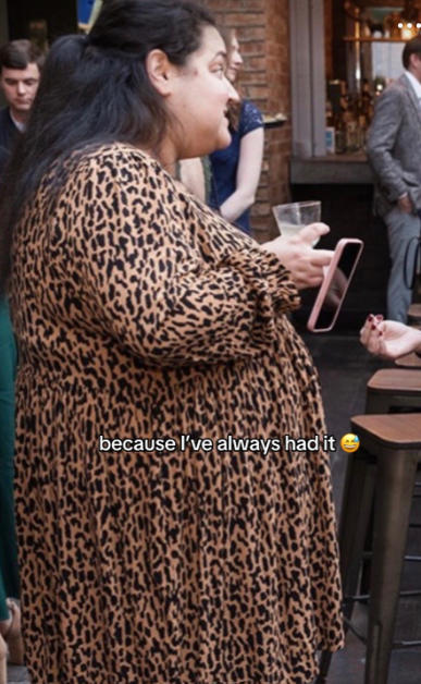 A woman in a leopard print dress holding a drink and phone.