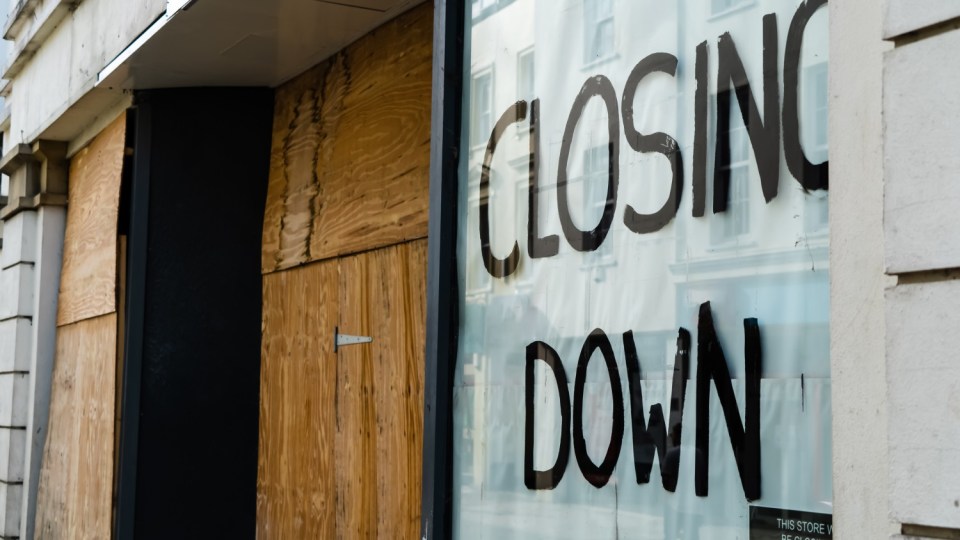 A store window with "CLOSING DOWN" painted on it, next to boarded-up windows.