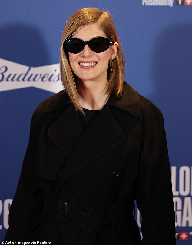 Rosamund cut a chic figure in a black trench which was cinched at her waist with a belt and accessorised with shades and a cream leather handbag
