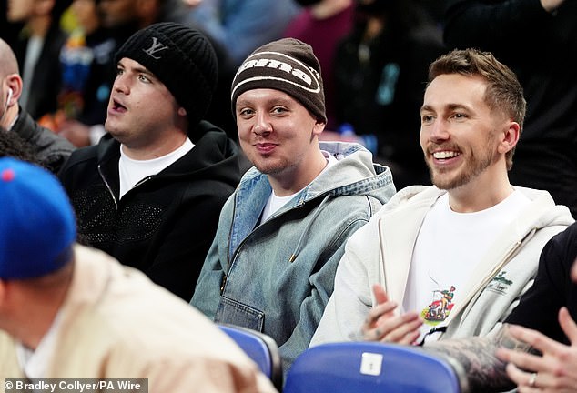 The rapper (centre) donned a beanie hat and denim jacket while joining pals to watch the game