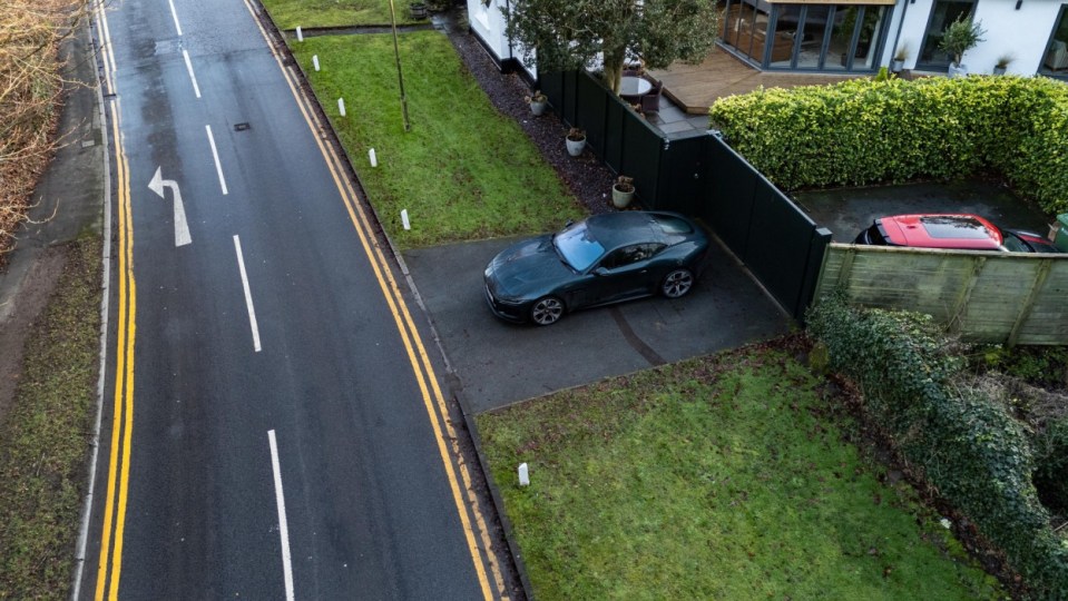 An aerial view of a green car parked in a driveway next to a road with double yellow lines.
