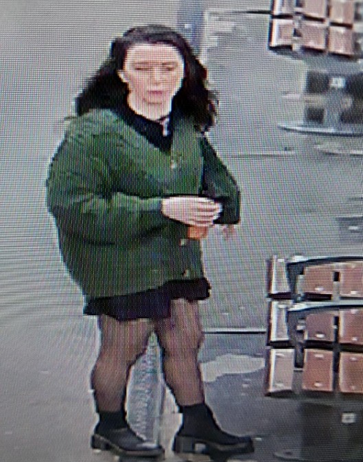 A woman in a green cardigan, black dress, tights, and boots holds a drink.