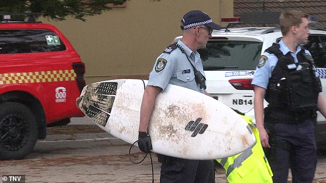 A police officer holds a surfboard after a 27-year-old man was attached at North Steyne Beach