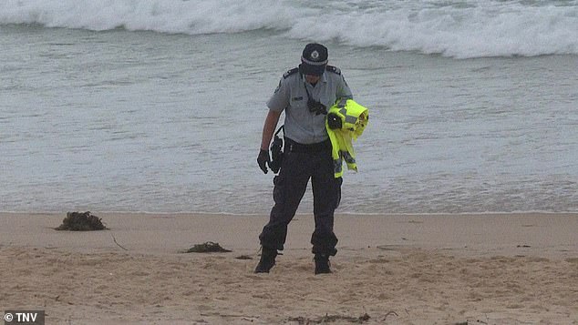 An officer is seen at the shore after the young man was mauled by a shark