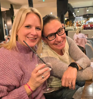 Two women smiling in a restaurant, one holding a drink.