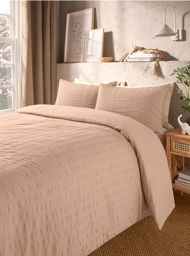 A bedroom featuring light pink bedding on a bed next to a window.