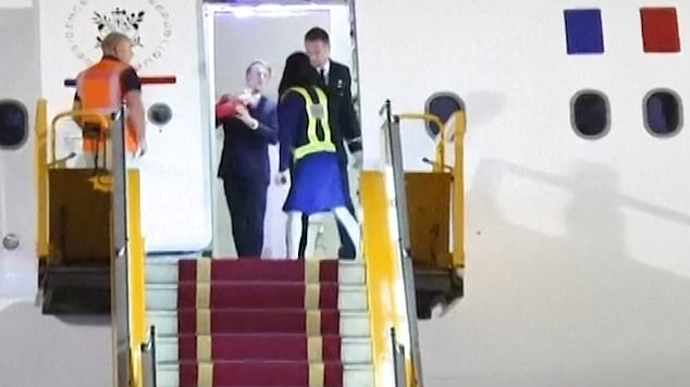 His wife Brigitte's arms emerge from the left of the open doorway, she places both hands on her husband's face and gives it a shove