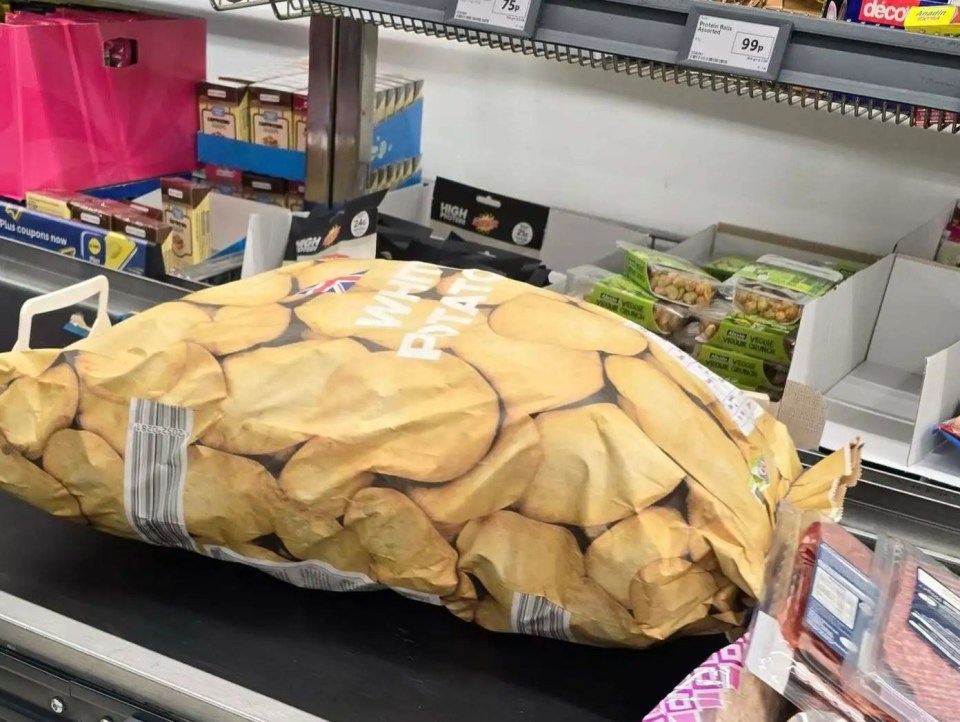 A large bag of potatoes on a checkout conveyor belt.
