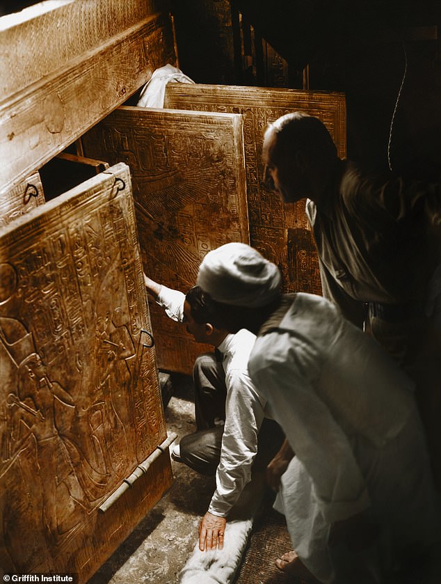 Howard Carter (kneeling) and some of his team looking through open doors of the four gilded shrines towards the quartzite sarcophagus within the tomb of Tutankhamun