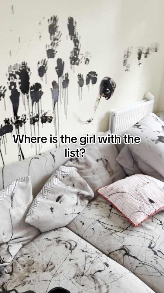 A living room with black handprints and paint splatters all over the white wall and sofa, making it a disaster zone.