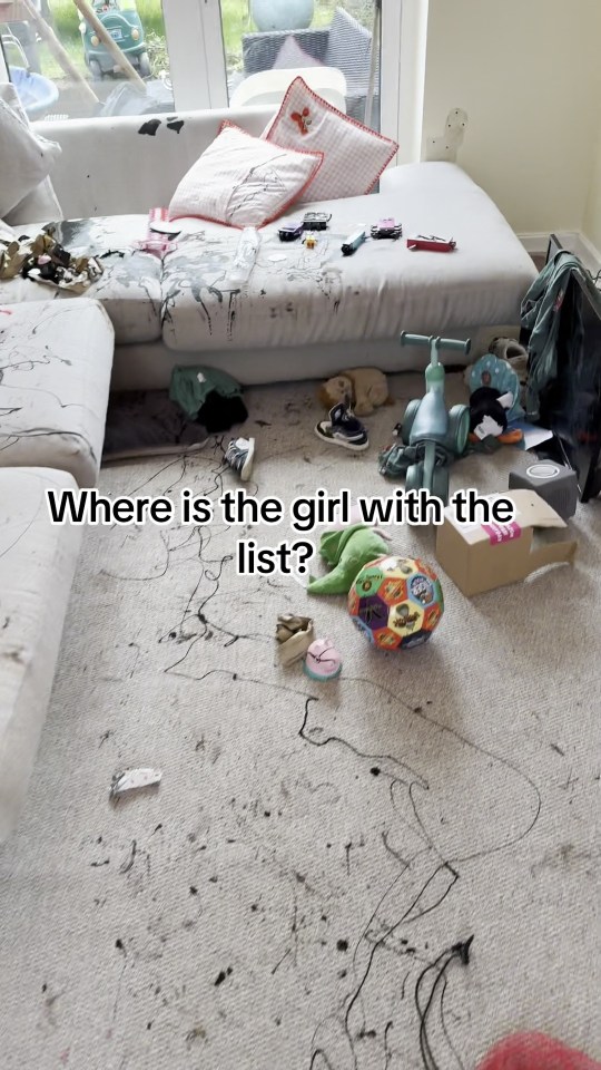 A living room with a white couch covered in ink splatters and toys, and the carpet also covered in ink and toys.