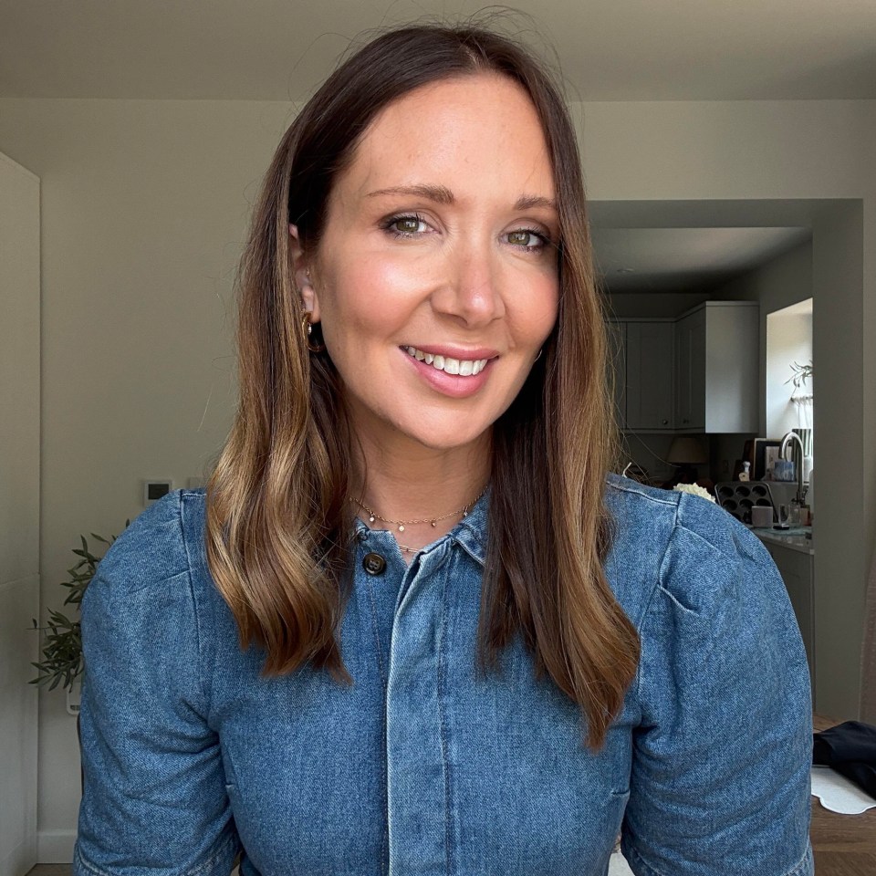 A woman with long brown hair smiles at the camera, wearing a denim top.