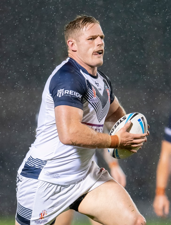 A rugby player from England wearing a white and blue jersey, holding a white rugby ball, and running in the rain.
