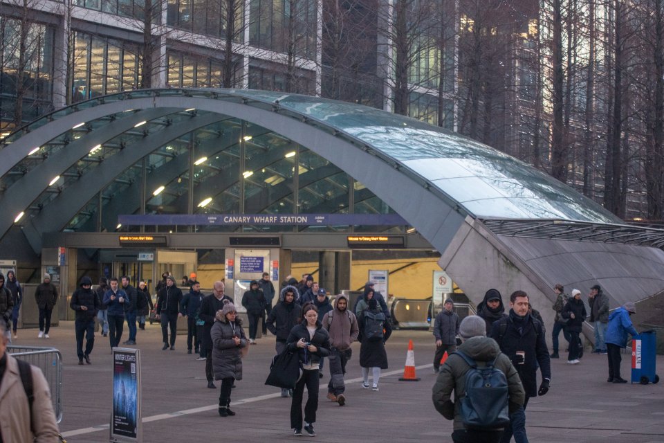 People walking outside the Canary Wharf Station, with its glass arch entrance visible, in London.