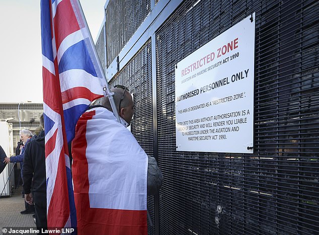 A man with a Union Flag is seen standing in front of a gate protecting a restricted zone at Dover Docks