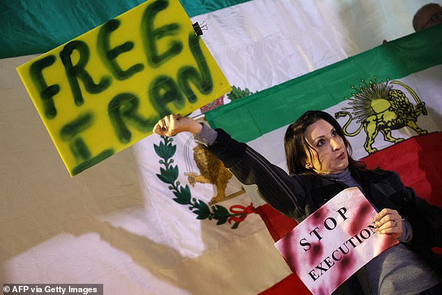A woman holds up a placard as she stands in front of a pre-1979 Islamic Revolution Iranian flag during a demonstration in solidarity with Iranian protestors, in Israel's central city of Holon on January 24, 2026