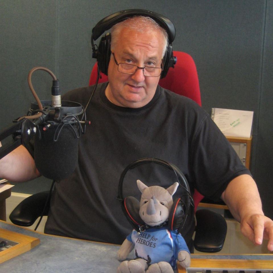 Man in a radio studio with a dog on his lap, both wearing headphones.