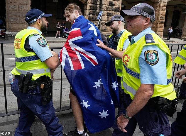 A man draped in an Australian flag is detained by police after an altercation during a "Invasion Day" rally and match on Australia Day in Sydney, Monday, Jan. 26, 2026. (AP Photo/Rick Rycroft)