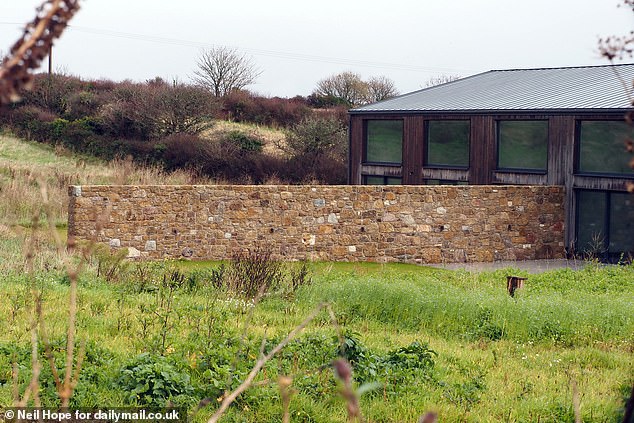 A mock-authentic Cornish stone wall juts out from the new modern barn at an angle