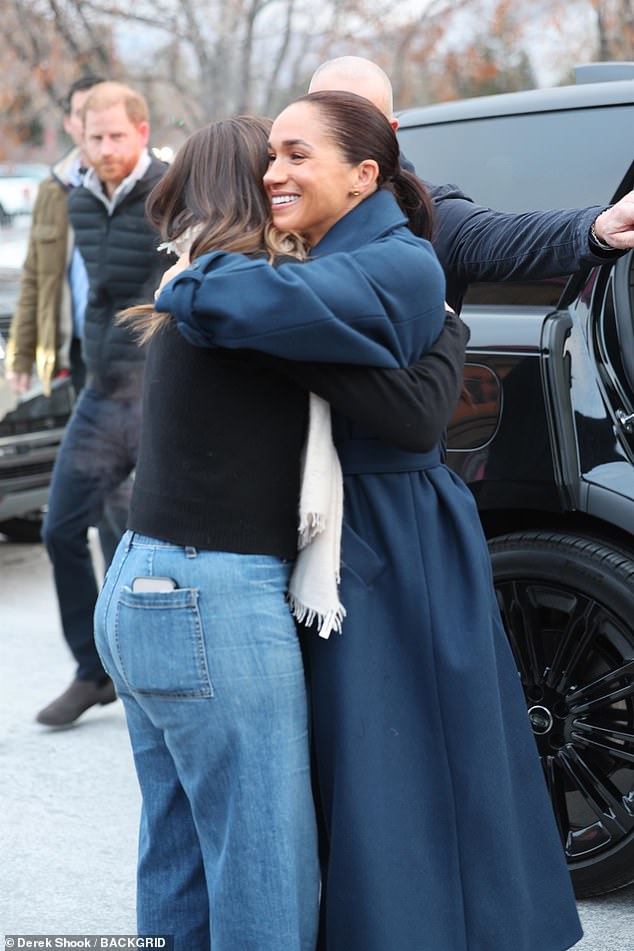 Meghan is hugged as she arrived at the screening yesterday with Harry in the background