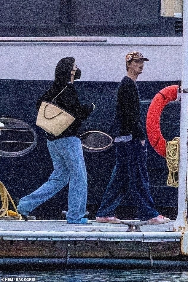 Jenner, 28, showed off her toned figure in a black triangle bikini top paired with loose black pants, at one point draping a sweatshirt around her waist as she checked her phone poolside