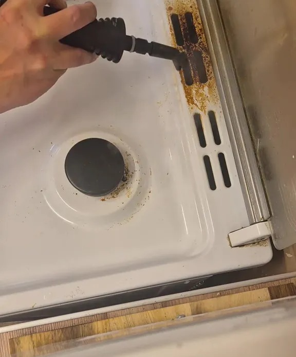 Cleaning a dirty oven with a steam cleaner.