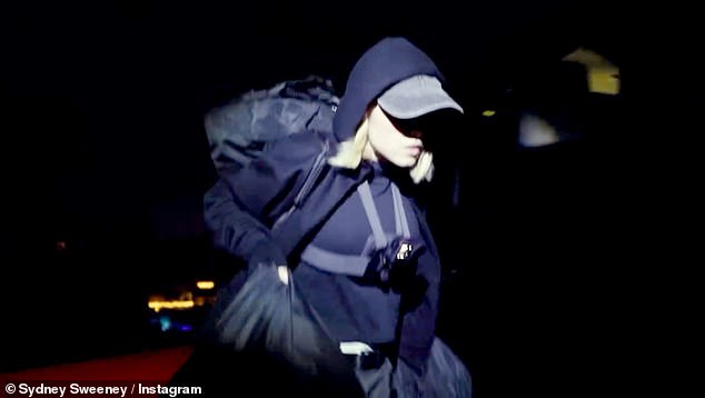 Sydney, dressed in all black, leads the way as the group scale the eight foot perimeter fence and climb the hill to the sign