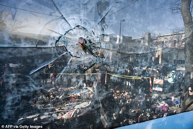 A gun shot perforation in a window pane can be seen in a window in front of a makeshift memorial for Alex Pretti