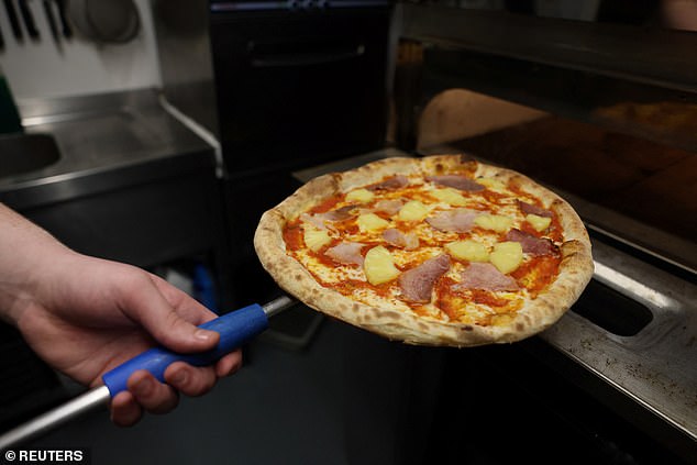 A ham and pineapple pizza coming out of a pizza oven. It has long been a debate whether the fruit belongs on the Italian foodstuff. Over half of Brits asked said pineapple does belong on pizza